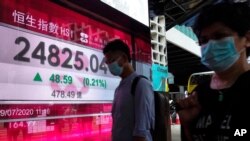 People wearing face masks walk past a bank's electronic board showing the Hong Kong share index in Hong Kong, July 29, 2020. 