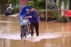 A woman pushes a child on a bicycle through a flooded street in Quang Tri.