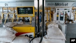 FILE - A gas station pump is fortified with sand bags as a Ukrainian serviceman exits a store in Kostiantynivka, Donetsk region, eastern Ukraine, Aug. 15, 2022. 