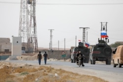 FILE - Russian and Syrian national flags flutter on military vehicles near Manbij, Syria, Oct. 15, 2019.