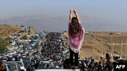 FILE - This UGC image posted on Twitter reportedly on Oct. 26, 2022, shows an unveiled woman overlooking thousands making their way toward a cemetery in Mahsa Amini's hometown. An increasing number of women in Iran are defying Iran's compulsory dress code by not wearing hijabs. 