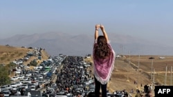 FILE - This UGC image posted on Twitter reportedly on Oct. 26, 2022 shows an unveiled woman standing atop a vehicle as thousands make their way towards a cemetery near Mahsa Amini's hometown to mark 40 days since her death.