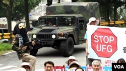 Manifestantes reclaman en Corea del Sur contra los ejercicios militares, mientras un vehículo militar estadounidense pasa frente al grupo.