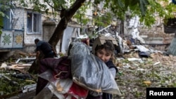 A woman carries her belogings out of a residential building destroyed by a strike in Mykolaiv, Ukraine, amid Russia's invasion of Ukraine, Sept. 11, 2022. 