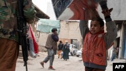 A boy carries a tin trunk past a Taliban guard outside a workshop in Kabul on Nov. 15, 2022.
