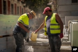 Builders share a water jug as they work in Madrid, July 10, 2023. Temperatures are rising during a heatwave scorching southern Europe.