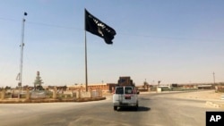 FILE - A vehicle passes by a flag of the Islamic State group in central Rawah, 281 kilometers northwest of Baghdad, Iraq. 