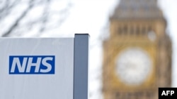 FILE - An NHS (National Health Service) sign is seen at St. Thomas Hospital, with the Big Ben clock face and the Elizabeth Tower in the background, in London, Jan. 13, 2017.