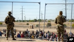 ARCHIVO - Migrantes esperan en fila junto a la valla fronteriza bajo la vigilancia de la Guardia Nacional de Texas para ingresar a El Paso, Texas, el 10 de mayo de 2023.