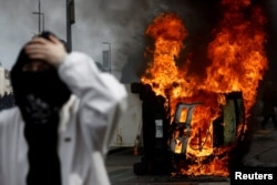 FILE - A masked protester stands in front of a burning car during clashes at a demonstration as part of the 10th day of nationwide strikes and protests against French government's pension reform in Nantes, March 28, 2023.