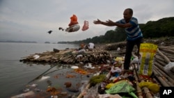 FILE - A Hindu devotee throws flowers and plastic bags into Brahmaputra river in Gauhati, India, Oct. 9, 2019. Negotiators at UNESCO in Paris discuss ways to end plastic pollution.