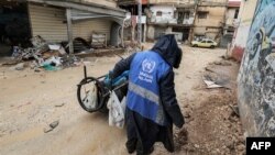 A man collects trash while wearing a jacket bearing the logo of the United Nations Relief and Works Agency for Palestine Refugees in the Near East along a street in the city of Jenin in the occupied West Bank on Jan. 30, 2024.