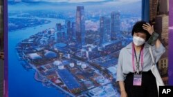 A woman wearing a mask stands near a board displaying a city landscape in Shanghai, July 6, 2023. China reported that 239 people died from COVID-19 in June in a significant uptick months after it lifted most containment measures. 