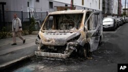 A man walks past a burned van on the aftermath of protests in Colombes, outside Paris, July 1, 2023.