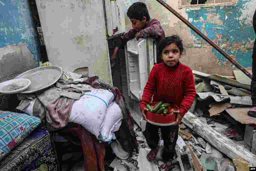 A child carries vegetables as another tries to salvage more from a refrigerator inside their damaged home, following overnight Israeli bombardment in Rafah in the southern Gaza Strip, Feb. 25, 2024.