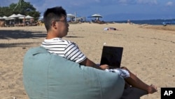 Армонио Лианг од Кина седи на плажа додека работи на својот компјутер во Бали, Индонезија, на 22 јуни 2023 година