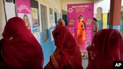 Women wait to cast their votes as one of them stands behind a selfie point during the first round of voting of India's national election in Behror, Rajasthan state, India, April 19, 2024.