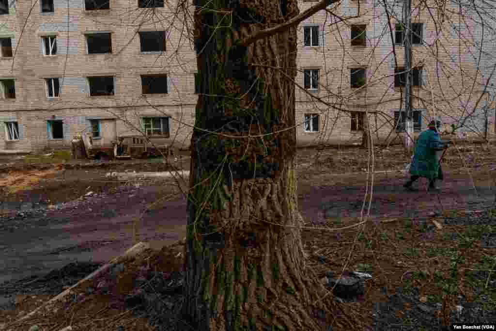 A woman passes by a destroyed car in one of the many streets that have been hit by Russian artillery in Siversk, April 4, 2023. 