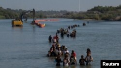 Una caravana pasa junto a una serie de boyas, que se construyen para disuadir a los migrantes de cruzar el río Grande, mientras buscan una abertura en el alambre de concertina para ingresar a Eagle Pass, Texas, EEUU, el 27 de julio de 2023.