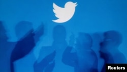 Archivo - Las sombras de las personas que sostienen teléfonos móviles se proyectan sobre un fondo con el logotipo de Twitter en esta imagen ilustrativa tomada en Varsovia el 27 de septiembre de 2013.