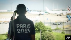 A Paris Olympics volunteer watches planes on the tarmac at Charles de Gaulle airport, July 19, 2024, in Roissy, north of Paris. Disruptions to airline operations stemming from a tech outage was causing delays at two major Paris airports.