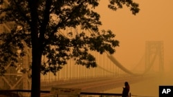 FILE - A man talks on his phone as he looks through the haze at the George Washington Bridge in Fort Lee, N.J., June 7, 2023.