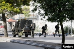 Israeli soldiers run next to an army vehicle in the Balata refugee camp in Nablus, amid the ongoing conflict between Israel and the Palestinian Islamist group Hamas, in the Israeli-occupied West Bank, Nov. 23, 2023.