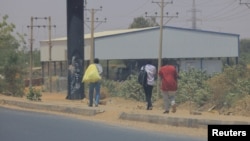 People cross the Halfaya Bridge as smoke rises in the background during clashes between the Sudanese army and paramilitary forces, as seen from Khartoum North, Sudan, April 15, 2023. 