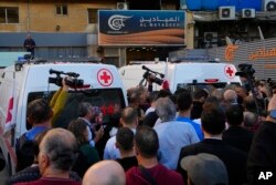 Journalists and family members gather by Lebanese Red Cross ambulances carrying the bodies of the two slain journalists of Pan-Arab TV network Al-Mayadeenm, outside the station's headquarters in Beirut, Lebanon, Nov. 21, 2023.