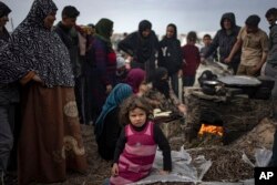 A little girl sits as Palestinians displaced by the Israeli bombardment wait for their turn to bake bread at the makeshift tent camp in the Muwasi area in Rafah, Gaza Strip, Saturday, Dec. 23, 2023.