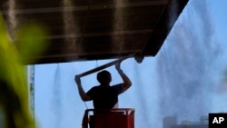 Un hombre trabaja afuera bajo los rociadores, el jueves 13 de julio de 2023 en el centro de Phoenix, Arizona, que está siendo azotado con temperaturas de más de 40 grados Celsius y advertencias de calor excesivo. (Foto AP/Matt York)