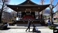 FILE - A woman pushes her child past a hall displaying 'hina' dolls at a Shinto shrine in Tokyo, March 3, 2023.