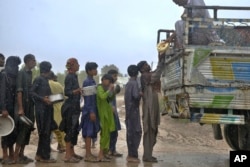 People stand in line to get free food distributed by volunteers outside a camp of internally displaced people from coastal areas due to Cyclone Biparjoy approaching, in Sujawal, Pakistan's southern district in the Sindh province, June 15, 2023.