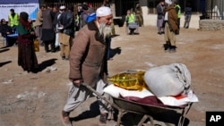 FILE - An Afghan man carries supplies in a wheelbarrow during a distribution of aid in Kabul, Feb. 16, 2022. U.S. officials, in recent talks with Taliban leaders, noted data indicating falling inflation and growing trade in Afghanistan in 2023.