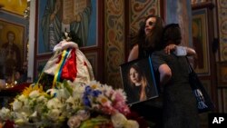 Mourners hug while olding a photo of Ukrainian writer Victoria Amelina during a memorial service for Amelina in Kyiv, Ukraine, July 4, 2023. 