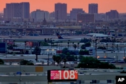 FILE - A sign displays an an unofficial temperature as jets taxi at Sky Harbor International Airport at dusk, July 12, 2023, in Phoenix.