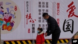 一名男子带着小女孩走过北京街头一面中国政府的宣传社会主义核心价值观的宣传墙。（2021年3月7日）