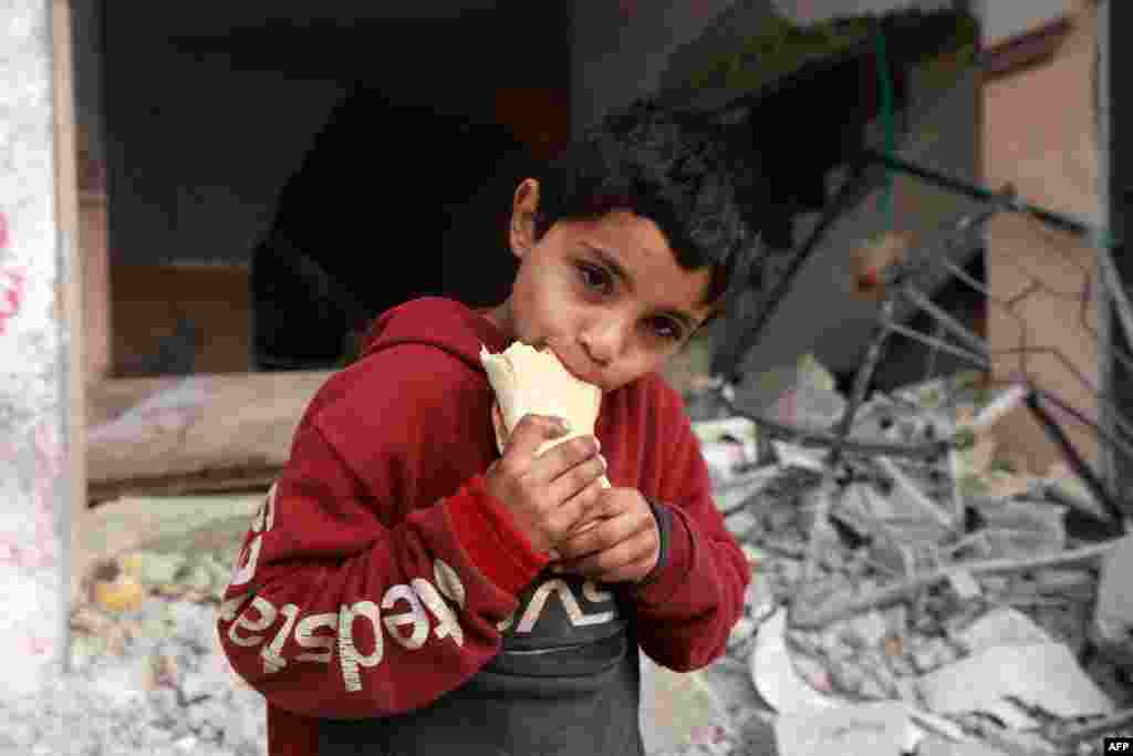 A child eats a sandwich in front of a building damaged by Israeli bombardment in Rafah in the southern Gaza Strip, Feb. 25, 2024.