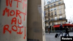 People walk past graffiti reading "Death to the King" the day after clashes during protests over French government's pension reform in Paris, March 24, 2023.