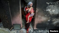 Souhila Belkati carries her child inside her burnt house following a wildfire in Bejaia, Algeria, July 25, 2023. 