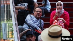 A woman cools herself off with a fan while sitting down in the Time Square area of New York City, June 18, 2024.
