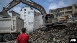 FILE - A construction worker sprays water as diggers remove the rubble of collapsed buildings, five months after a 7.8-magnitude jolt and its aftershocks wiped out swathes of Turkey's mountainous southeast, in Samandag on July 9, 2023. 