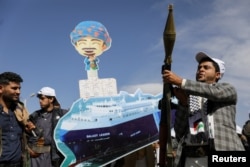 A Houthi follower holds a rocket launcher as others carry a cutout banner portraying the Galaxy Leader cargo ship that was seized by Houthis, during a parade as part of a "popular army" mobilization campaign, in Sanaa, Yemen, Feb. 7, 2024.