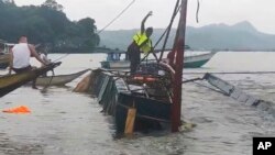 A man stands on a capsized passenger boat as they undergo rescue operations at Binangonan, Rizal province, east of Manila, Philippines, July 27, 2023. (Philippine Coast Guard via AP)