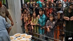 Women and children wait for free food at a distribution point in Lahore, Pakistan, June 27, 2023.