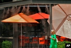 Una mujer camina bajo los chorros de agua afuera de un restaurante, el 12 de julio de 2023 en Gilbert, Arizona.