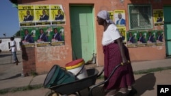 FILE - An elderly woman pushes a wheelbarrow past campaign posters in Mabvuku on the outskirts of Harare, Zimbabwe, Dec. 9, 2023. 