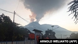 Pengendara berkendara saat Gunung Lewotobi Laki-Laki mengeluarkan asap panas di Flores Timur, Nusa Tenggara, Timur, 2 Januari 2024. (Foto: AFP/ARNOLD WELIANTO)