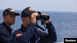 FILE PHOTO: A Philippine Coast Guard personnel looks through binoculars while conducting a resupply mission for Filipino troops stationed at a grounded warship in the South China Sea, Oct. 4, 2023. 