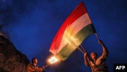 FILE - An Iraqi Kurd holds a Kurdish flag while another holds lit torches during celebrations of Noruz (Nowruz), the Persian new year, in the town of Akra, in Iraq's northern autonomous Kurdish region, on March 20, 2022.